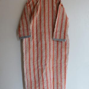 May include: A long, patterned robe with vertical stripes in shades of orange and cream. The robe has long sleeves and a gray collar and cuffs. The fabric appears to be lightweight, suitable for layering or warmer weather.