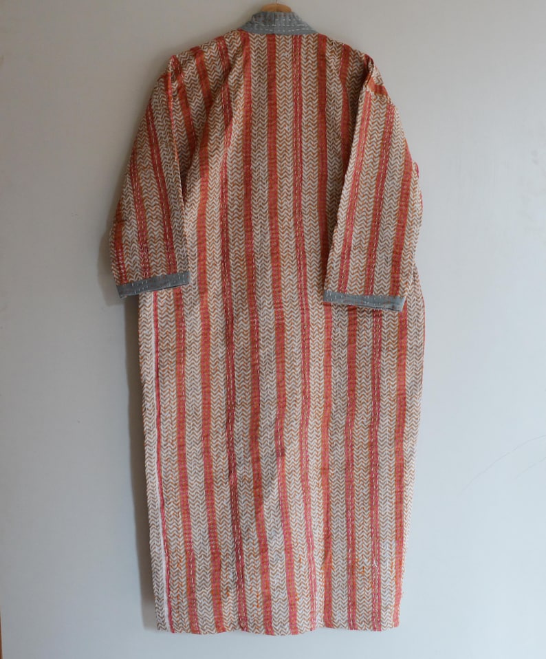 May include: A long, patterned robe with vertical stripes in shades of orange and cream. The robe has long sleeves and a gray collar and cuffs. The fabric appears to be lightweight, suitable for layering or warmer weather.