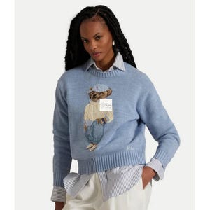 May include: A light blue long-sleeve knit sweater featuring a crew neckline and a ribbed hem. The center displays an embroidered teddy bear wearing a cream sweater, blue cap, and blue pants. The letters RL are embroidered in white at the bottom right.