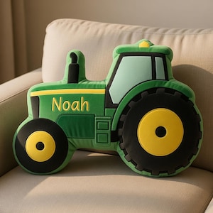 Puede incluir: Un cojín verde con forma de tractor, con ruedas negras y detalles amarillos. El nombre "Noah" está bordado en amarillo. El cojín está diseñado para parecerse a un tractor, adecuado para decoración o niños.