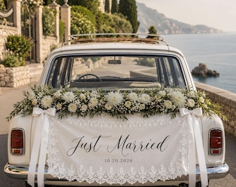Pode incluir: Um carro antigo branco decorado com um arranjo floral de dálias brancas e folhagem. Uma faixa de tecido creme com acabamento em renda pende da mala, apresentando o texto preto Just Married e a data 20/10/2026 com fitas brancas.