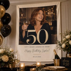 May include: A large rectangular fabric banner featuring a portrait of a person holding a champagne glass, with the large gold number 50, the text FIFTY NEVER LOOKED SO GOOD, Happy Birthday, Sophia!, and the date 08.24.20XX printed on the lower section.