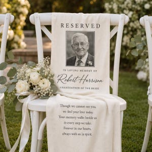 May include: A white fabric memorial sign draped over a white chair, featuring the text RESERVED, a black and white portrait of Robert Harrison, the words IN LOVING MEMORY OF, and a poem. A bouquet of white roses and baby's breath is attached.