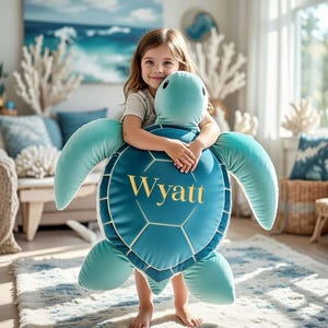 May include: A teal turtle-shaped cushion with the name "Wyatt" embroidered in gold. The cushion features a geometric pattern on its back and large flipper-like appendages. The image shows a child hugging the cushion, suitable for a child's bedroom or nursery.