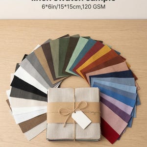 Puede incluir: Muestras de tela de lino en varios colores, incluyendo beige, gris, verde y marrón. Las muestras están dispuestas en forma de abanico, con una pila de muestras beige atadas con hilo y una etiqueta en blanco. El texto "linen swatch sample" está en la parte superior.