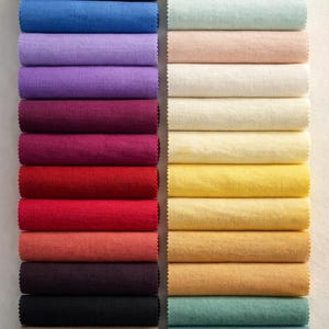 May include: A collection of rolled fabric samples in various colors. The left side features deep shades like navy, purple, and red. The right side showcases lighter hues, including cream, yellow, and teal. The fabric appears to be linen or a similar textured material.