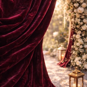 May include: A deep burgundy velvet curtain drapes elegantly, its folds catching the light. In the background, a floral archway and lanterns create a romantic ambiance. The scene suggests a wedding or special event setting.
