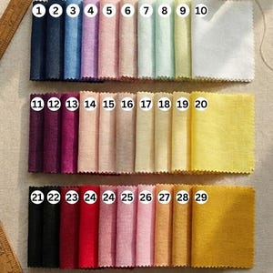 May include: A collection of fabric swatches in various colors, numbered 1 through 29. The swatches are arranged in three rows, showcasing a range of hues from dark blues and purples to pinks, yellows, and oranges. A wooden spool of thread and a ruler are also present.