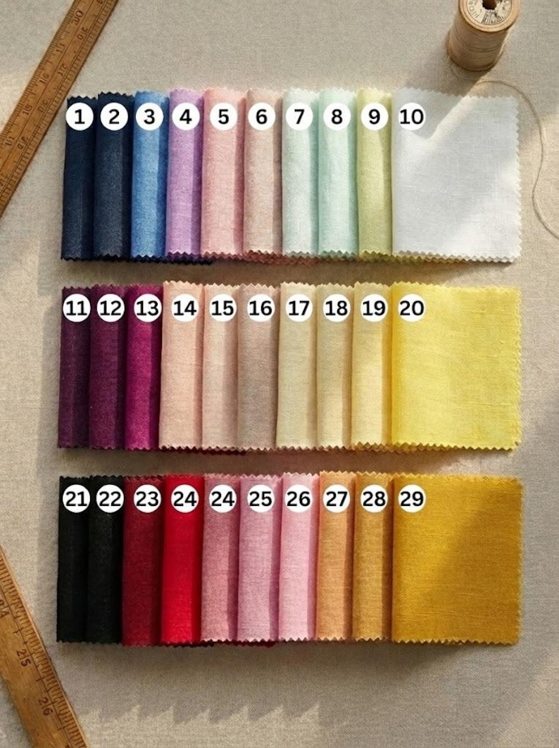 May include: A collection of fabric swatches in various colors, numbered 1 through 29. The swatches are arranged in three rows, showcasing a range of hues from dark blues and purples to pinks, yellows, and oranges. A wooden spool of thread and a ruler are also present.