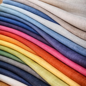Puede incluir: Una pila de muestras de tela coloridas en varios tonos, desde beige hasta azul marino. La disposición muestra un degradado de colores, incluyendo azules, rosas y verdes. Ideal para diseño textil y manualidades.