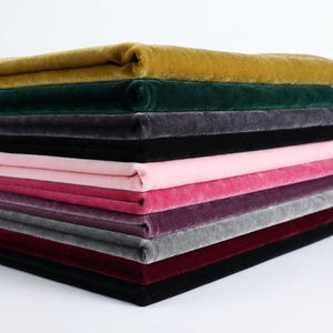 Puede incluir: Una pila de piezas de tela de terciopelo dobladas en varios colores, incluyendo amarillo mostaza, verde oscuro, gris carb&oacute;n, negro, rosa claro, magenta, morado intenso, gris claro y burdeos, con una textura suave de pelo corto.