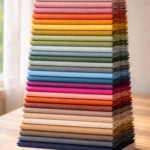May include: A stack of fabric swatches in a variety of colors, including beige, pink, orange, yellow, green, blue, and purple. The swatches are neatly arranged, showcasing the different hues and textures of the fabric.