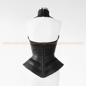 May include: Black leather corset with a high collar and a zipper closure. The corset features a structured design with horizontal and diagonal panels, creating a fitted silhouette. The garment is displayed on a white mannequin.