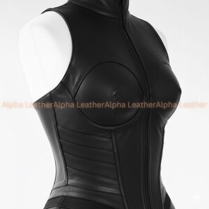 May include: A black leather corset with a high collar and a full-length zipper. The corset features a structured bodice with molded cups and horizontal paneling. The text "Alpha Leather" is printed in a light orange color.