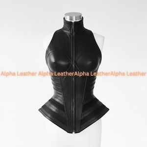 May include: A black leather corset with a high collar and a full-length zipper. The corset features a structured design with panels and a fitted waist. The text "Alpha Leather" is visible in the image.