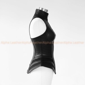 May include: A black leather corset with a high collar and a zipper closure. The corset has a structured design with horizontal and vertical panels, and a sleeveless design. The text "Alpha Leather" is visible in the background.