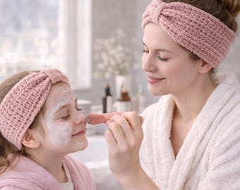 May include: A woman and a child wearing matching pink knitted headbands. The child has a white face mask applied, and the woman is applying more with a pink brush. Both are in bathrobes.