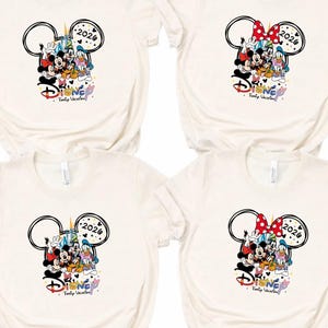 May include: Four cream-coloured t-shirts with a Disney-themed graphic. The design includes Mickey Mouse ears, various Disney characters, the year "2026," and the word "Disney" in a colourful font. One shirt has a red and white polka-dot bow.