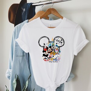 May include: White t-shirt with a Disney-themed graphic. The design includes Mickey Mouse, Minnie Mouse, Donald Duck, and Goofy, with the text "Disney Family Vacation" and the year "2026" inside a Mickey Mouse head outline.