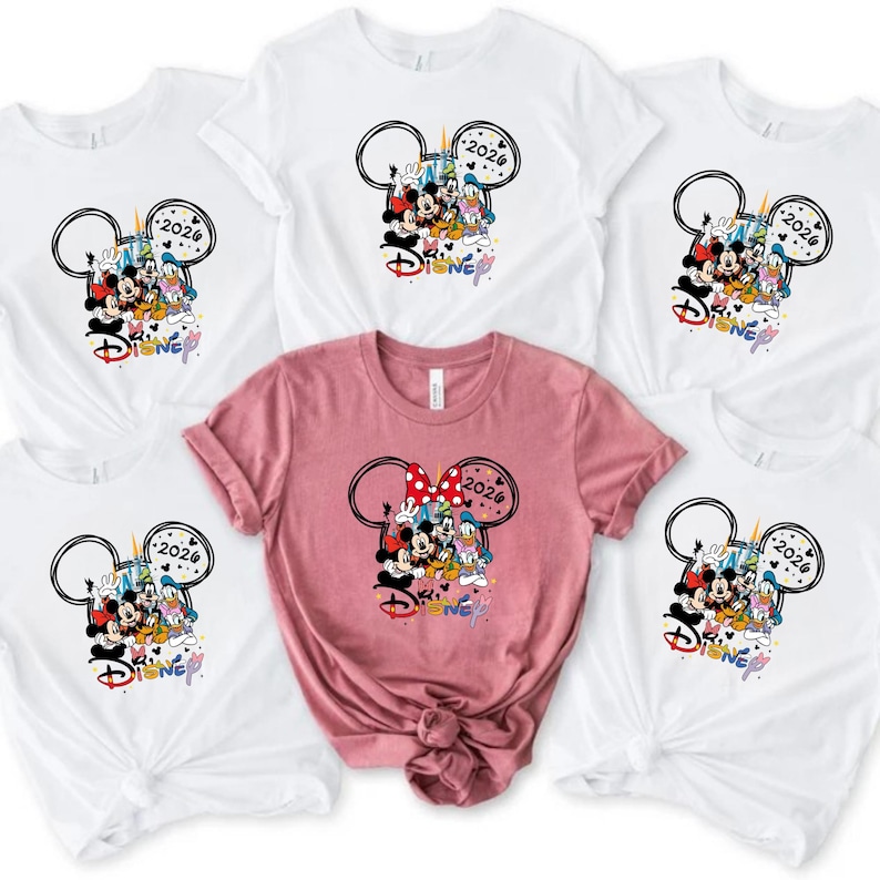 May include: White and pink t-shirts with a Disney design. The design features Mickey Mouse, Minnie Mouse, Donald Duck, and other characters, with the year 2026. The word "Disney" is also present in a colourful font.