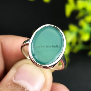 Könnte beinhalten: Ein silberner Ring mit einem ovalen, hellgrünen Stein. Der Stein ist in eine silberne Lünette gefasst und hat eine glatte Oberfläche. Der Text "ShineSocietyIndia" ist auf dem Stein sichtbar. Der Ring wird von Fingern gehalten.
