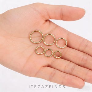 May include: Six gold-coloured hoop rings of varying sizes are displayed in an open hand. The rings are circular and appear to be made of metal. The text "ITEZAZFINDS" is visible at the bottom of the image.