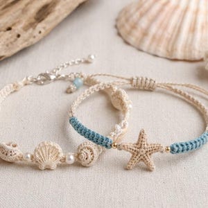 Può includere: Due braccialetti fatti a mano a tema spiaggia. Un braccialetto presenta ciondoli a forma di conchiglia e perle, mentre l'altro ha un ciondolo a forma di stella marina e accenti blu. Entrambi sono realizzati con un uncinetto color crema.