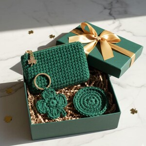 May include: A green crochet gift set, including a zippered pouch with a gold shamrock charm, a four-leaf clover keychain, and a coaster, presented in a green gift box with a gold ribbon. The box is filled with shredded paper.