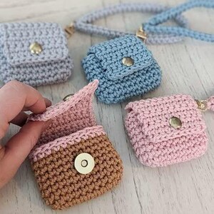 May include: Crocheted mini pouches in various colors: gray, blue, and pink. One pouch is open, revealing a pink interior and brown exterior. Each pouch has a button closure and a small strap or cord. The pouches are handmade.