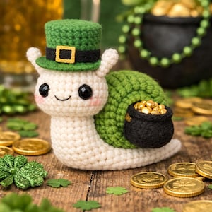 Könnte beinhalten: Eine gehäkelte Schnecke mit einem grünen Koboldhut mit goldener Schnalle, die einen kleinen schwarzen Topf mit Goldmünzen trägt. Die Schnecke befindet sich auf einer Holzoberfläche mit Goldmünzen und Kleeblättern.
