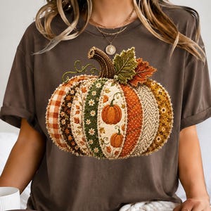 May include: A dark brown short-sleeve t-shirt featuring a large, central graphic of a pumpkin composed of various patterned fabric segments in shades of orange, green, and cream, with a small text label reading Expresso in the corner.
