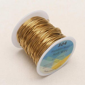 Puede incluir: Un carrete de alambre blando de acero inoxidable 304 de color dorado. La etiqueta indica un tamaño de 1,0 mm. El alambre está enrollado en un carrete de plástico blanco, para manualidades o joyería.