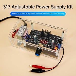 May include: A clear acrylic case houses a 317 Adjustable Power Supply Kit. The kit includes a black circuit board with electronic components, a digital display, and a knob. The text "Output DC 1.25V-12V adjustable between electronic DIY circuit learning" is visible.