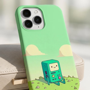 Puede incluir: Una funda de teléfono verde con una ilustración de dibujos animados de un robot verde y rectangular en un campo de hierba con nubes. La funda está diseñada para un teléfono inteligente con tres lentes de cámara. El robot tiene una cara sonriente y botones.
