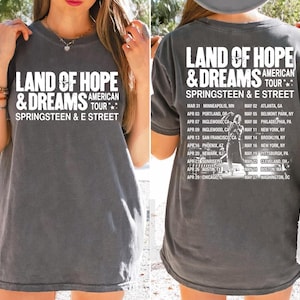 Puede incluir: Camiseta gris oscuro con la frase blanca "LAND OF HOPE & DREAMS AMERICAN TOUR SPRINGSTEEN & E STREET". La parte trasera muestra fechas y lugares de la gira. Una camiseta informal de estilo vintage.