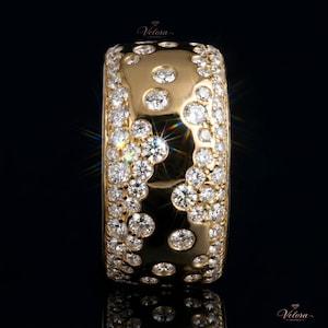 Puede incluir: Un anillo ancho, de color dorado, incrustado con numerosos diamantes pequeños y brillantes. El anillo presenta un diseño único con grupos de diamantes y piedras individuales más grandes. Sobre un fondo negro, se destaca su brillo.