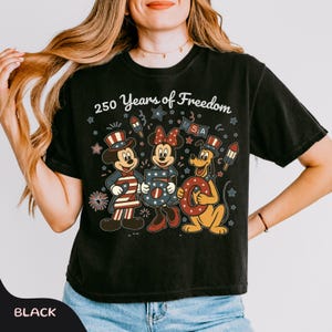 Może przedstawiać: Czarny t-shirt z Myszką Miki, Minnie i Pluto w patriotycznych strojach. Tekst "250 Years of Freedom" z gwiazdami, fajerwerkami i literami "USA".