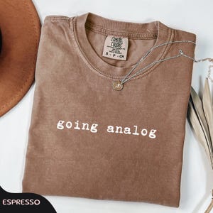 May include: A white ceramic mug with a black handle and the text "But First, Coffee" in a black, handwritten-style font. The mug is on a white surface.