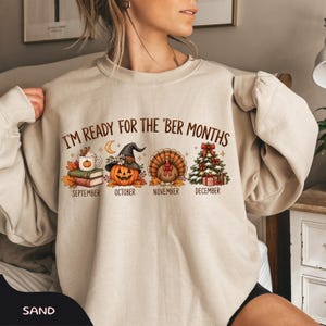 May include: A sand-colored crewneck sweatshirt featuring the text I'M READY FOR THE 'BER MONTHS. The graphic includes a mug on books for September, a jack-o'-lantern in a witch hat for October, a turkey for November, and a Christmas tree for December.