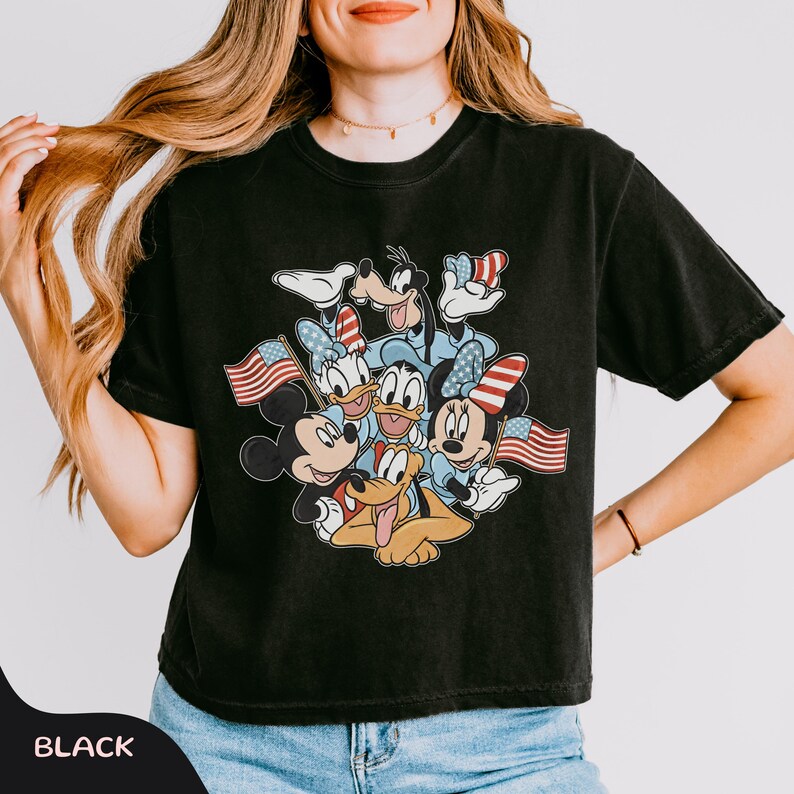May include: Black t-shirt featuring a graphic of Mickey Mouse, Minnie Mouse, Donald Duck, Daisy Duck, Goofy, and Pluto, each holding an American flag. The characters are in a patriotic design. The word "BLACK" is at the bottom.