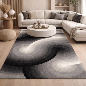 May include: A contemporary living space with a white corner sofa, a circular textured coffee table, and a rug with a swirling, monochrome design. The rug's pattern adds visual interest, harmonising with the room's neutral palette.