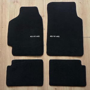 May include: A set of four black car floor mats. The mats are rectangular with rounded edges and feature the word "CIVIC" in white lettering. These mats are designed to protect the vehicle's interior.