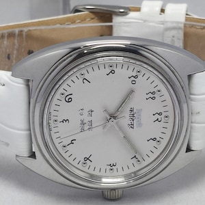 May include: A silver-toned wristwatch with a white face and a white leather band. The watch face features Arabic numerals and hands. The band is white with a textured pattern and a silver buckle.