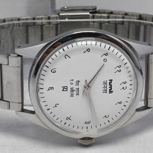 May include: A white ceramic mug with a black handle and the text "But First, Coffee" in a bold, black font. The mug is set against a blurred background, suggesting a cozy setting.