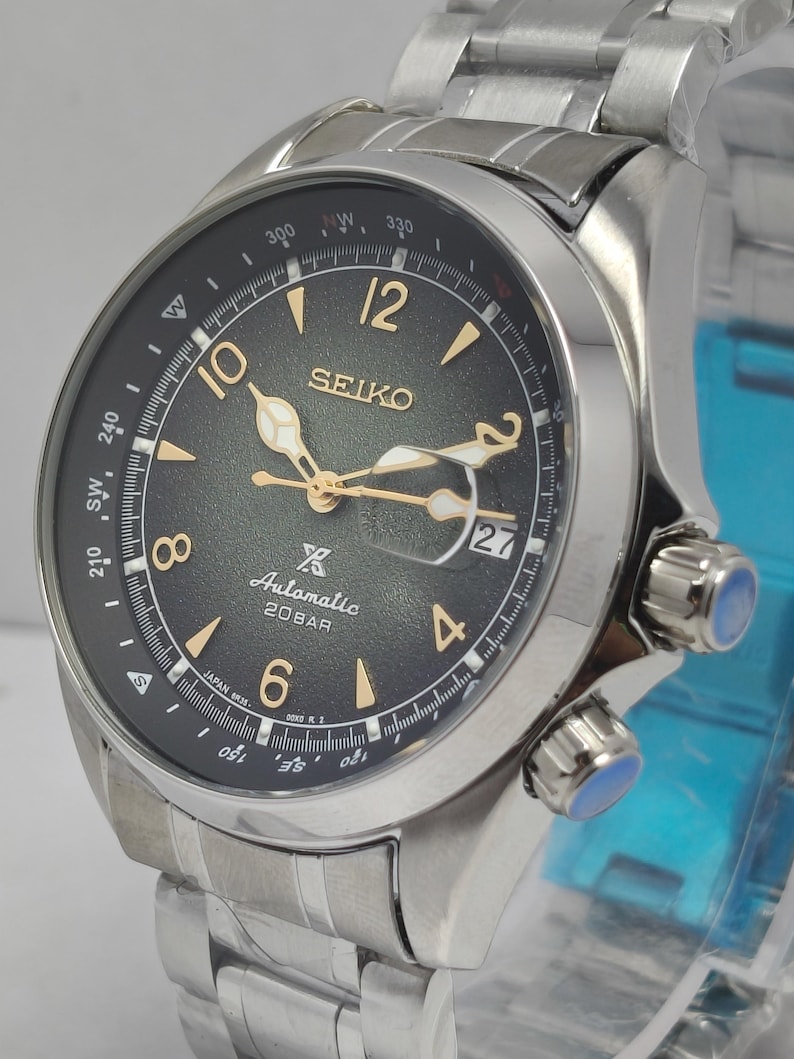 May include: A stainless steel Seiko automatic wristwatch with a black dial. The watch features gold-colored hands and hour markers, a date display, and a rotating bezel. The watch band is made of stainless steel.