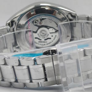 May include: Close-up of a silver-toned wristwatch with a metal band. The watch's back is visible, showcasing the inner workings and the text "SEIKO TWENTY-FOUR JEWELS JAPAN". The watch is secured with a clear plastic band.
