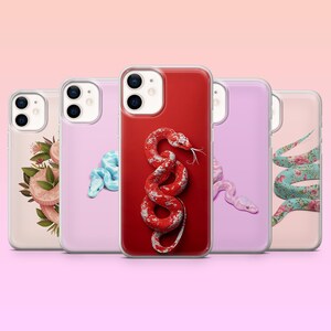 May include: A selection of phone cases with snake-themed designs. The cases showcase diverse snake illustrations in shades like red and blue, alongside floral patterns. The cases are arranged in a row against a pink backdrop.