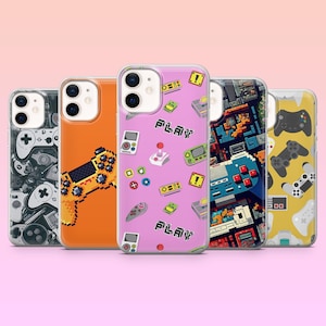 Puede incluir: Una colección de fundas para teléfonos con diseños temáticos de videojuegos. Las fundas presentan mandos pixelados, consolas de juegos y la palabra "PLAY". Los colores incluyen naranja, rosa, azul y amarillo. Las fundas están dispuestas sobre un fondo rosa.