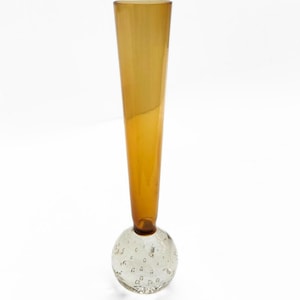 May include: An amber glass vase with a clear, bubble-filled spherical base. The vase has a slender, conical shape, widening towards the top. The base is a clear glass sphere with numerous small air bubbles, creating a unique texture.