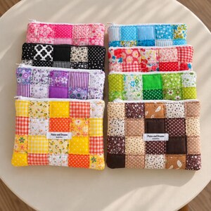Può includere: Otto astucci rettangolari con cerniera realizzati in tessuto trapuntato con vari motivi patchwork in rosa, nero, viola, giallo, blu, rosso, verde e marrone. Ogni astuccio presenta un'etichetta bianca con il testo Pixies and Dreams by luvinbox.